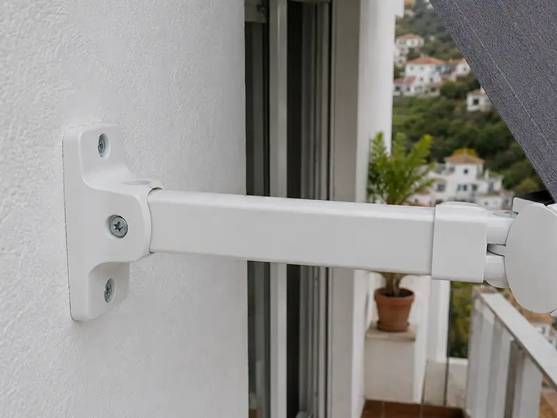 Detalle del brazo articulado y soporte de un toldo punto recto instalado en Málaga sobre una ventana con estructura de aluminio lacado.