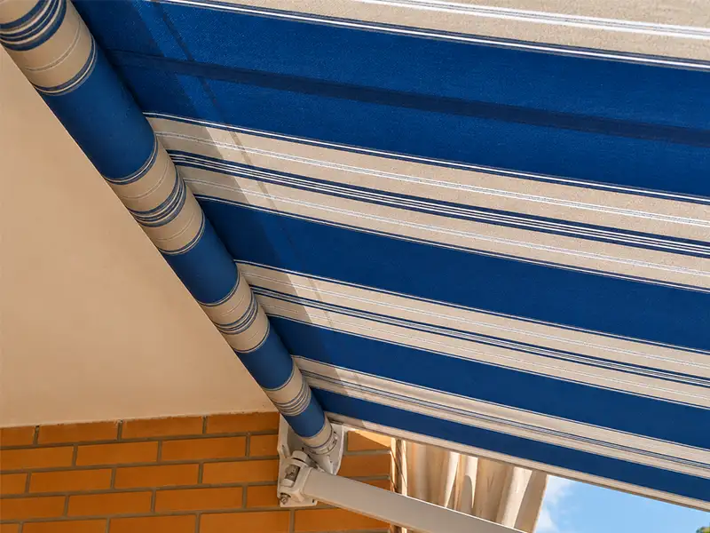 Detalle de toldo de brazos articulados con lona a rayas azules y beige instalado en vivienda en Málaga.