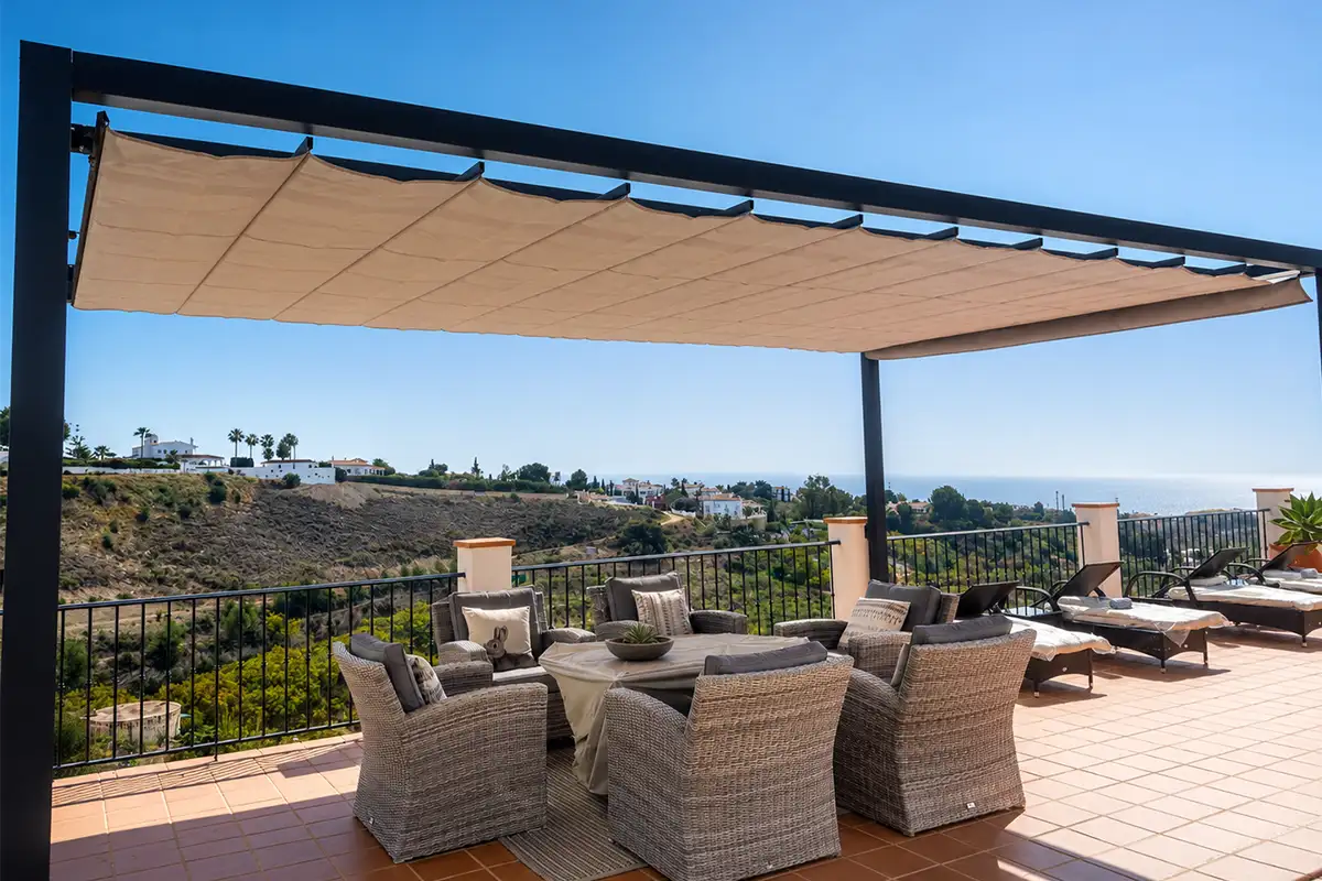 Pérgola de aluminio con toldo corredero de lona color arena instalada en una terraza con vistas al mar en Málaga.