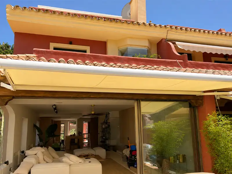 Toldo de brazos articulados con cofre y lona color arena instalado en terraza de vivienda en Málaga.