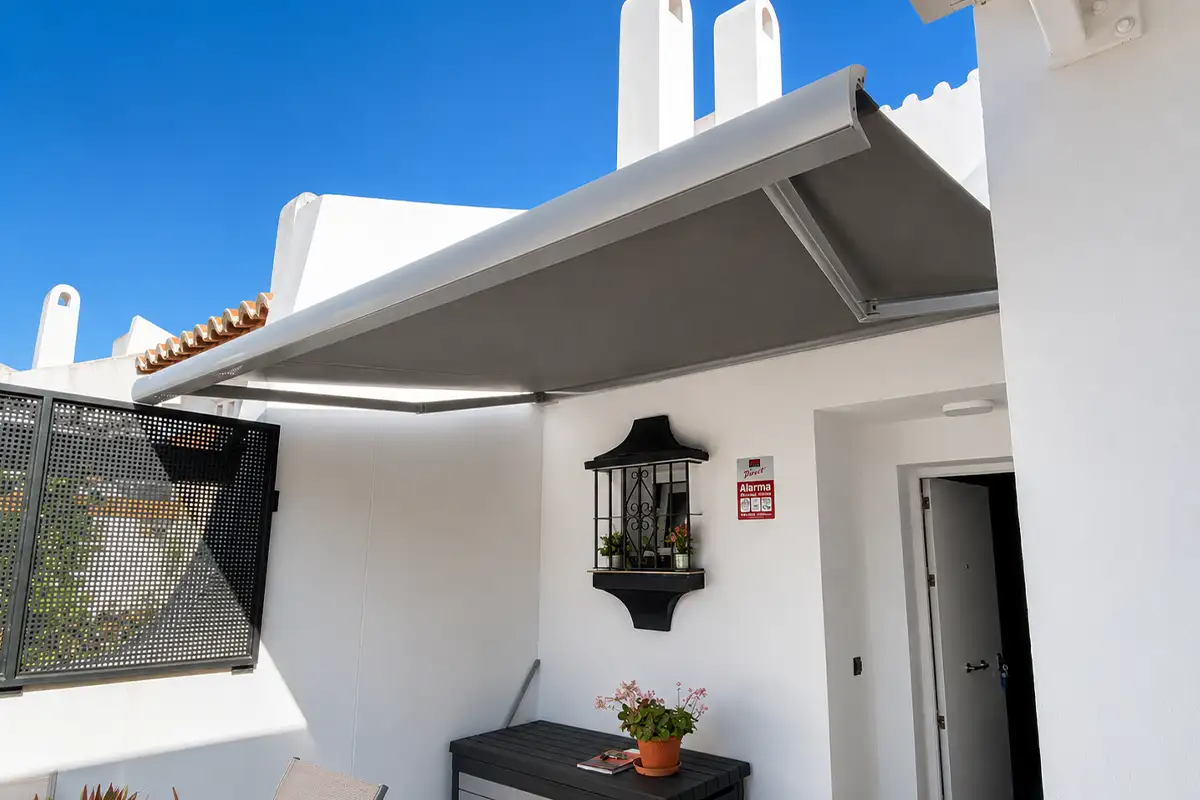Toldo articulado con cofre y lona gris instalado en terraza de vivienda en Málaga.