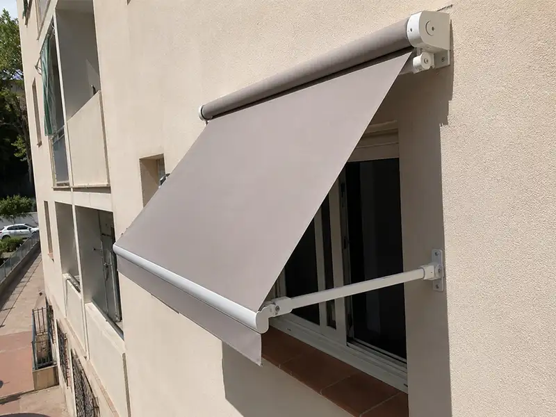 Toldo punto recto con cofre y brazos laterales instalado sobre una ventana en la costa de Granada para proporcionar protección solar y reducir el calor en el interior.