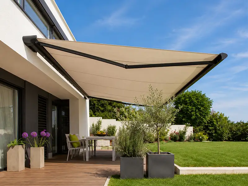 Toldo articulados con cofre y lona color arena instalado en terraza de jardín en Málaga.