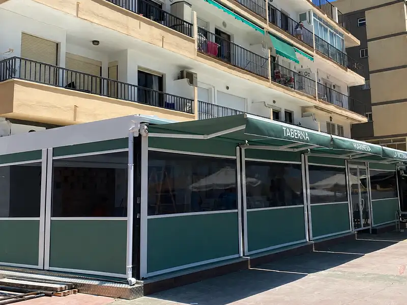 Toldo cortavientos con guías instalado en la terraza de un restaurante en Málaga para proteger del viento y ampliar el espacio exterior.