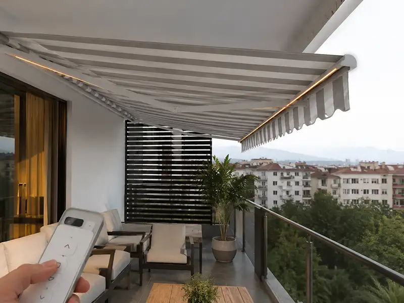 toldo articulado sin cofre automático con mando con lona blanca y rayas verdes en el balcón de casa en Málaga