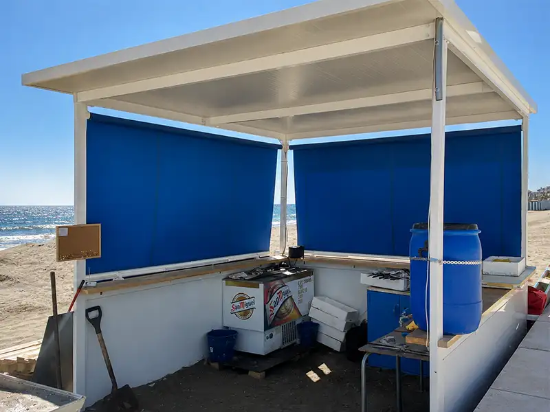 Toldo stor de lona azul instalada en un chiringuito de playa para proteger del sol, el viento y mejorar el confort del espacio.