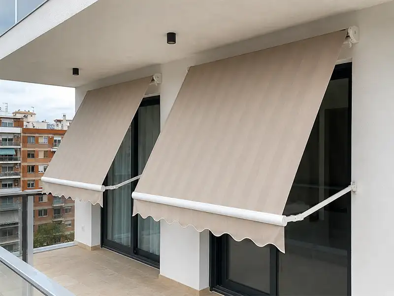 Toldos stor enrollables con lona de rayas beige instalados en un balcón de edificio para proteger del sol y aumentar la privacidad.