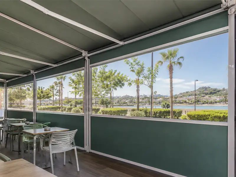 Interior de terraza de restaurante con toldo cortavientos de lona y ventana transparente, ofreciendo protección frente al viento sin perder las vistas.