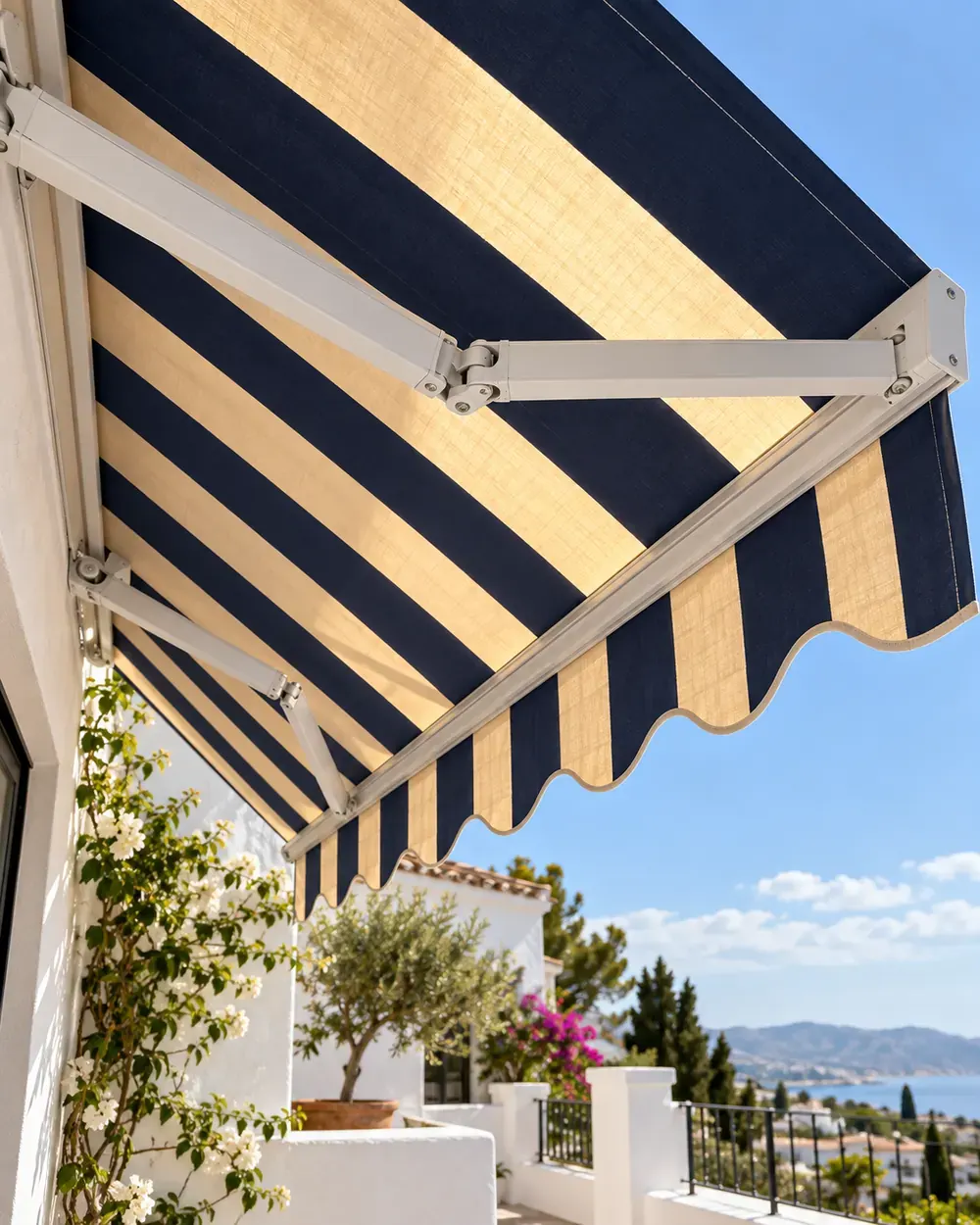 Brazos articulados de aluminio blanco y lona de rayas azul marino y arena de un toldo articulado vistos desde abajo