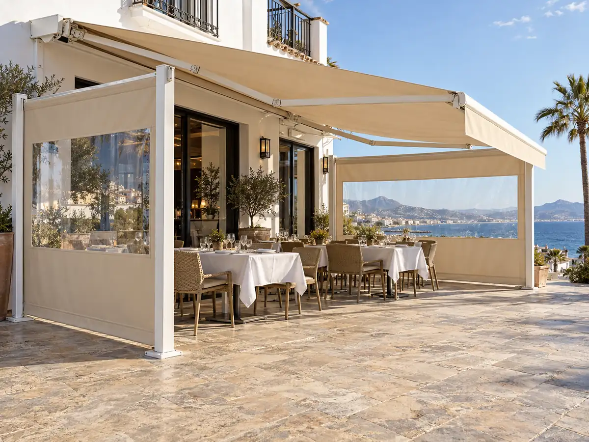 Toldo articulado y cortavientos para restaurante Toldo articulado con cortavientos laterales transparentes en la terraza de un restaurante con vistas al mar