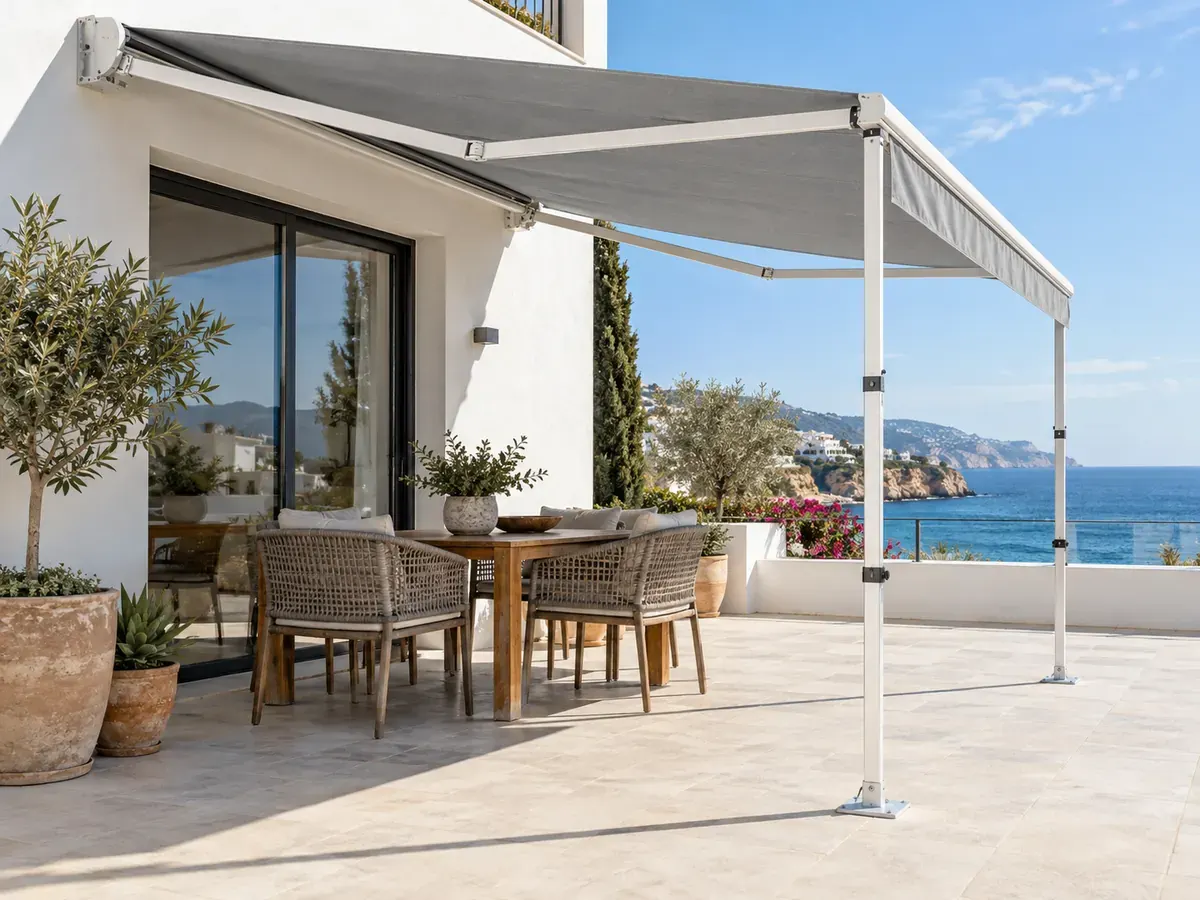 Toldo con patas para terraza Toldo articulado con patas telescópicas y lona gris en una terraza con jardín junto al mar